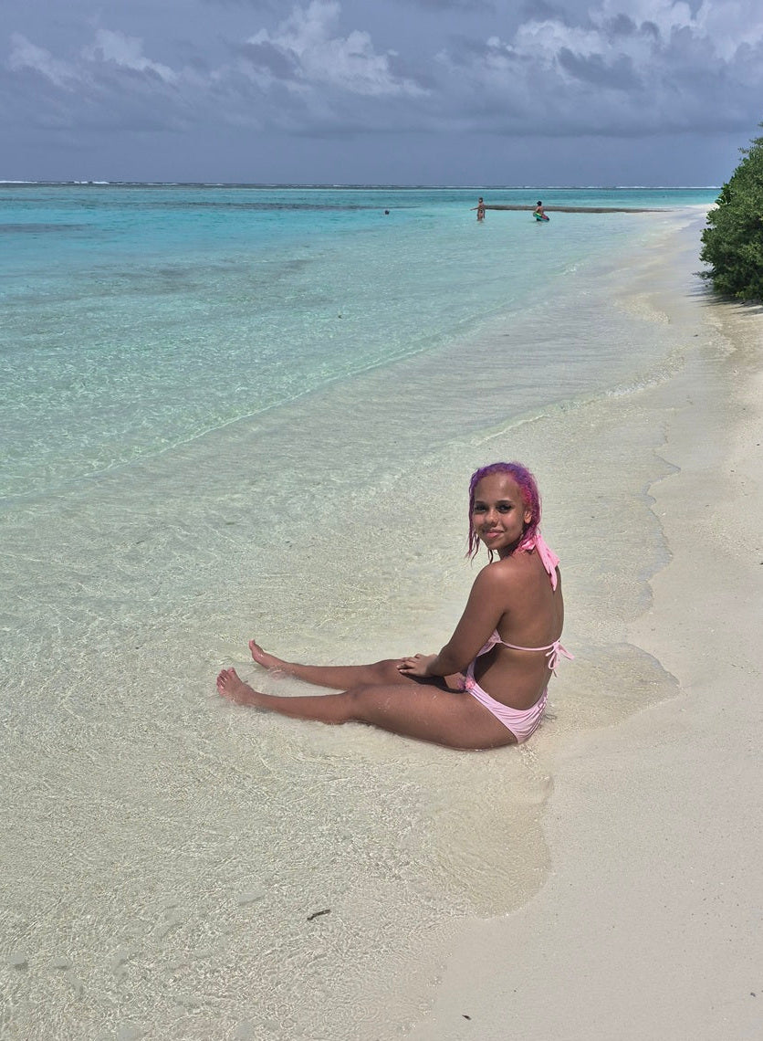 Baddie Betty sitting in the water on a beach on Cocoon resort in the Maldives, with turquoise water & soft sand.