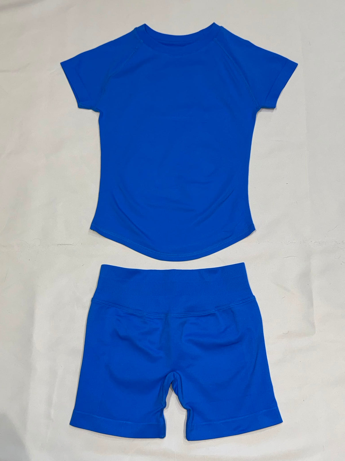 Pearl, Dazzling Blue Ladies Gym set. Short-sleeve top and matching high-waisted shorts with scrunch bum, laid flat.